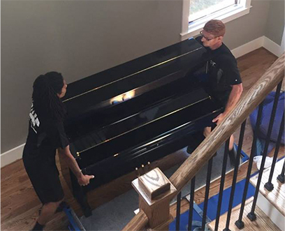 Two strong movers from the Birmingham team carrying a piano down the stairs of a customer's home.