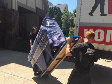 Two strong movers moving a piano carefully to a Motivated Movers Birmingham truck.