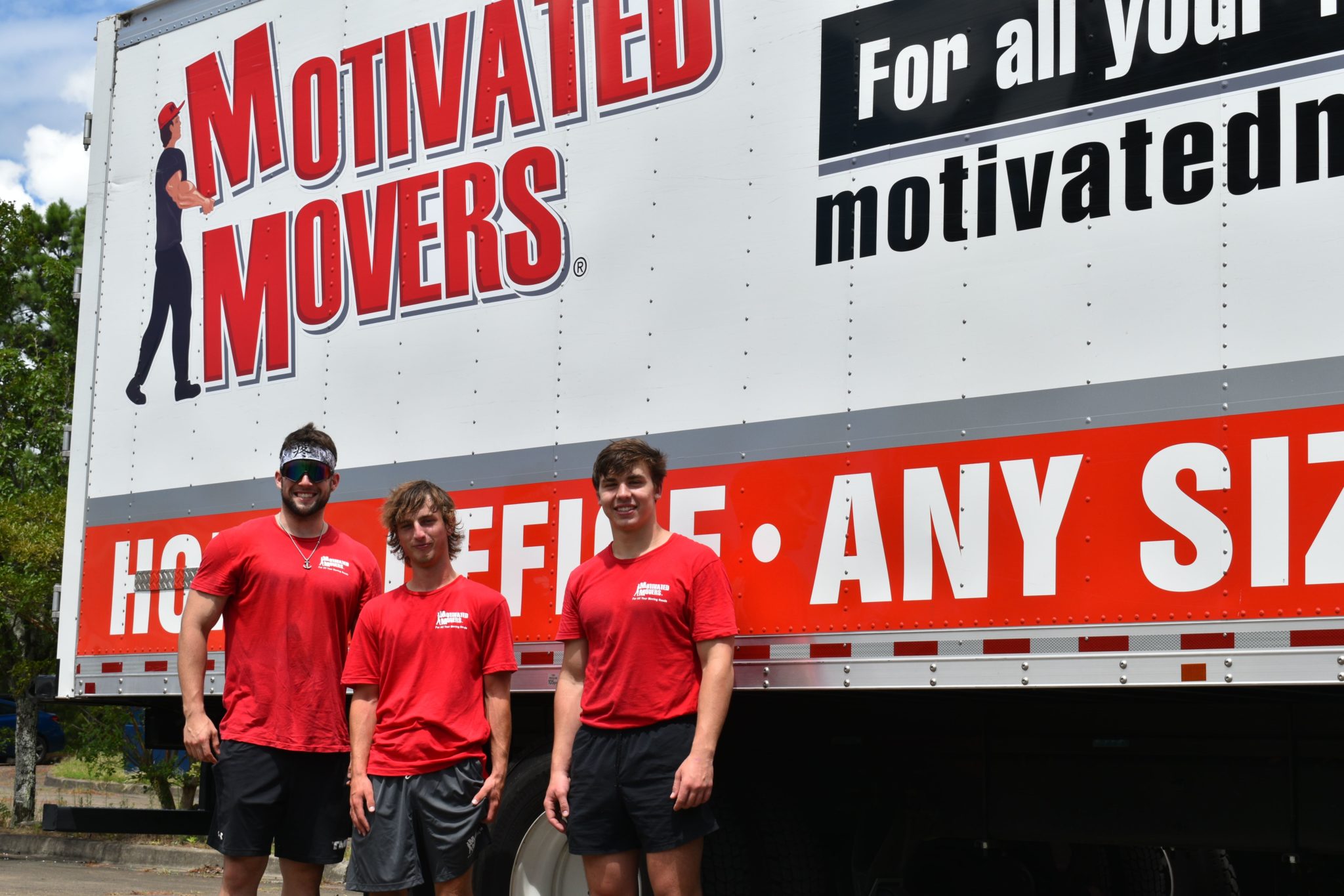 Three movers standing in front of a Motivated Movers Birmingham truck ready to serve