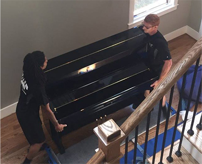 Two strong Motivated Movers from the Montgomery team carry a piano through the home of a customer.